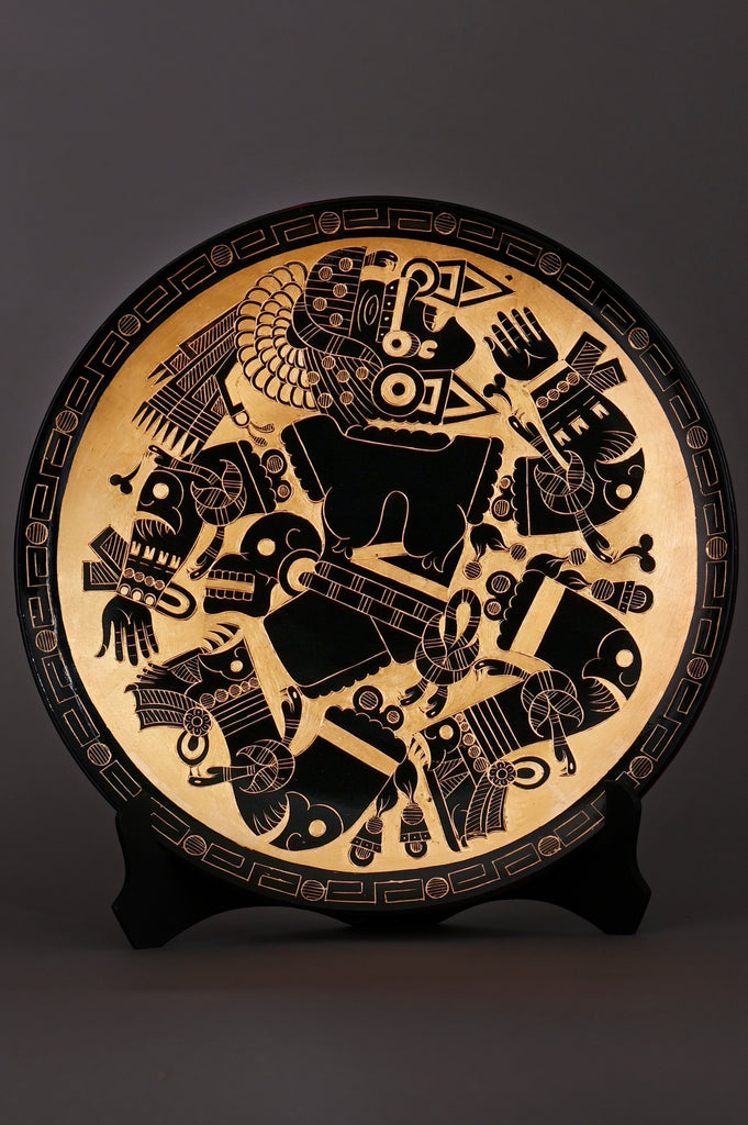Decorative plate with intricate black designs depicting the Aztec Moon Goddess on a gold leaf background.