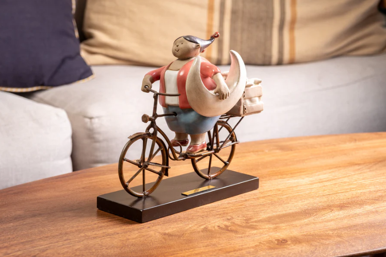 Handmade ceramic sculpture by Rodo Padilla of a woman holding the moon while riding her bike – 5.9 x 4.3 x 9.8 inches – whimsical Mexican folk art from the Gorditas collection celebrating dreams and joy.